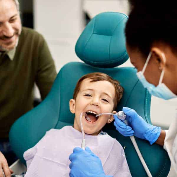 Boy in dental chair with parent watching dentist work