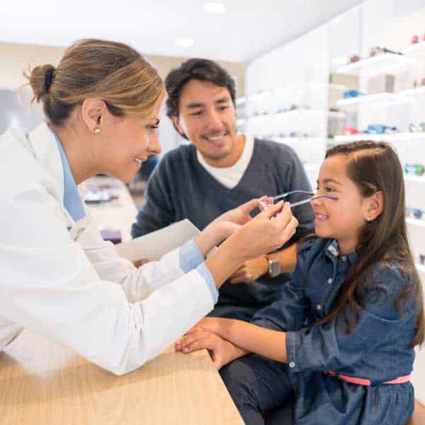 Happy girl at the optician's shop with her father and the eye doctor and trying new glasses