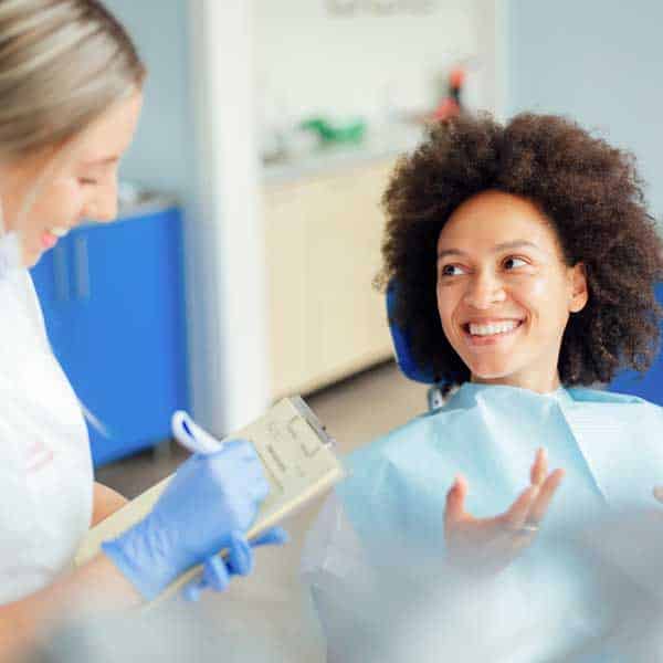 Caucasian female dental doctor taking notes in her notebook of her African American female patient while she's sitting in a dental chair